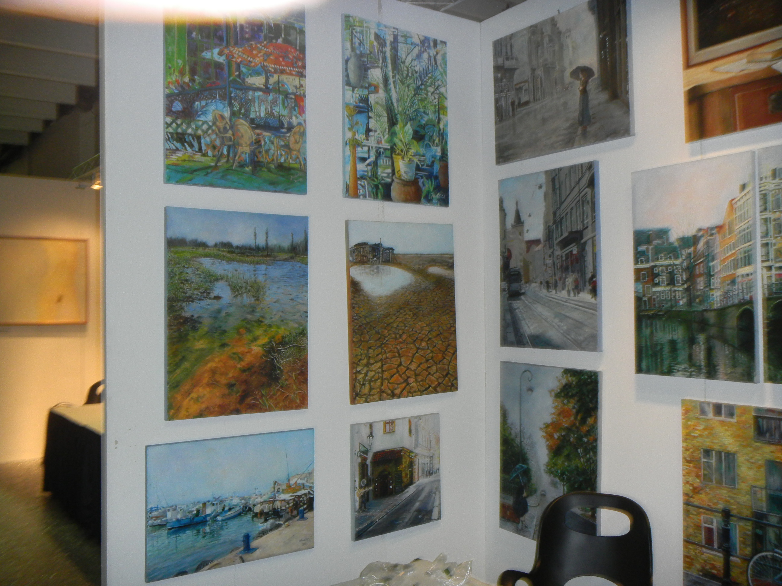 A close view of an ArtExpo display wall shows rows of landscape, still-life and city paintings mounted together.