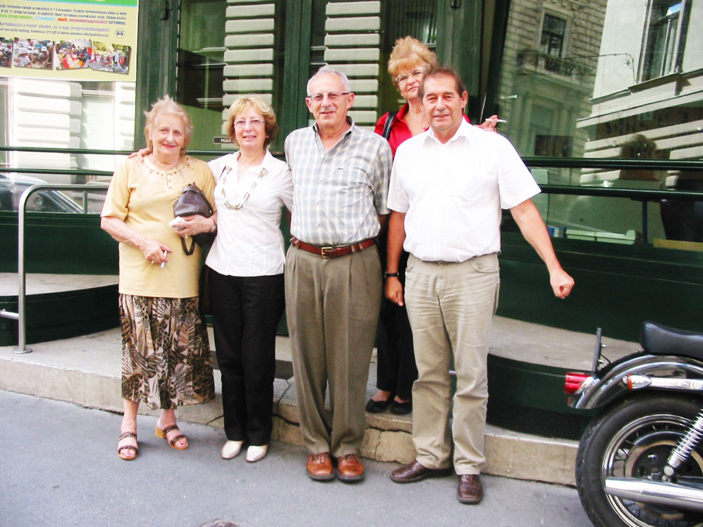 Five adults pose beside a glass railing and steps at the Balint House exhibition, with a wheelchair partly visible.