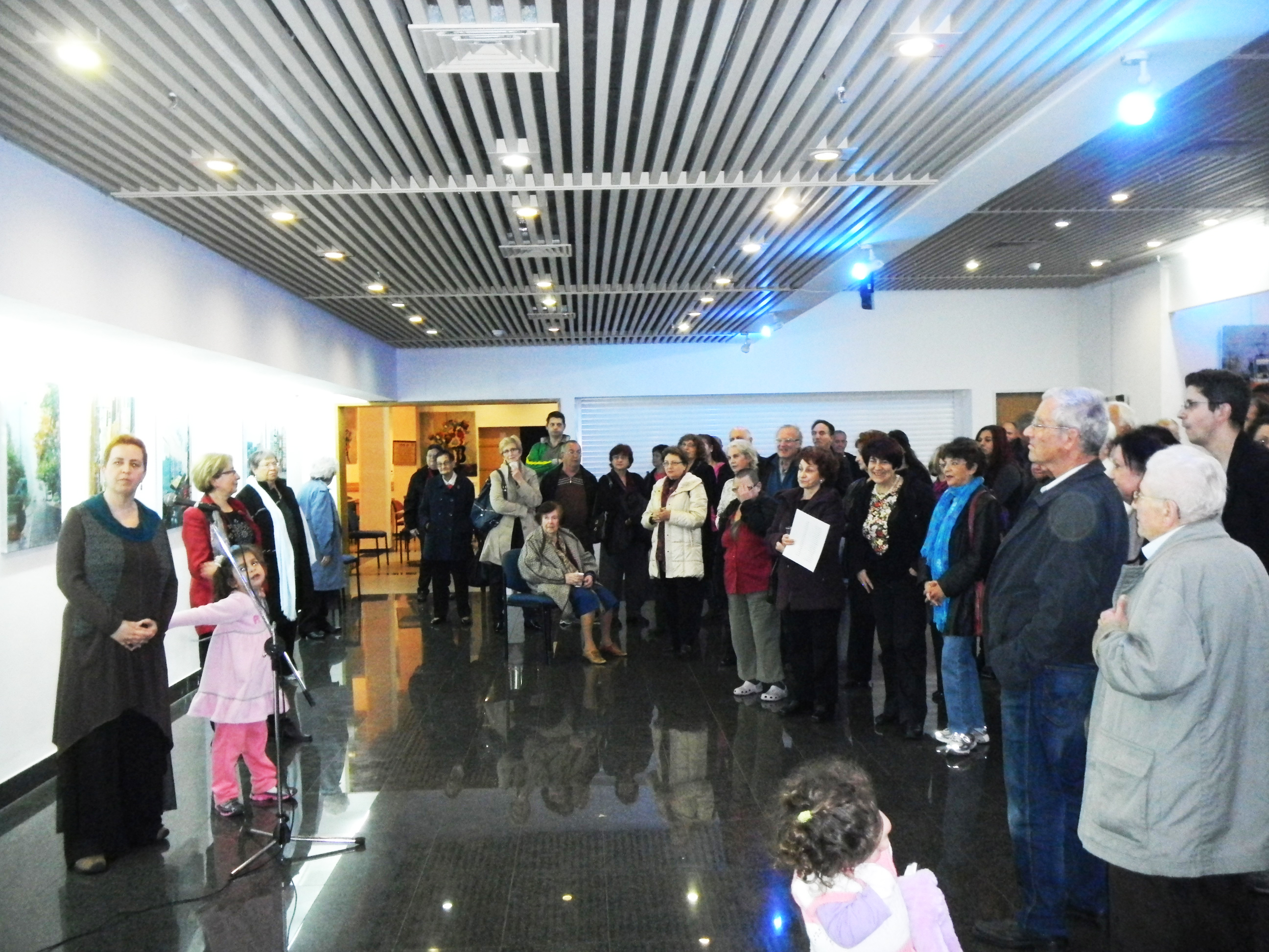 A large group of visitors listens to a speaker in a brightly lit gallery with paintings displayed around the room.