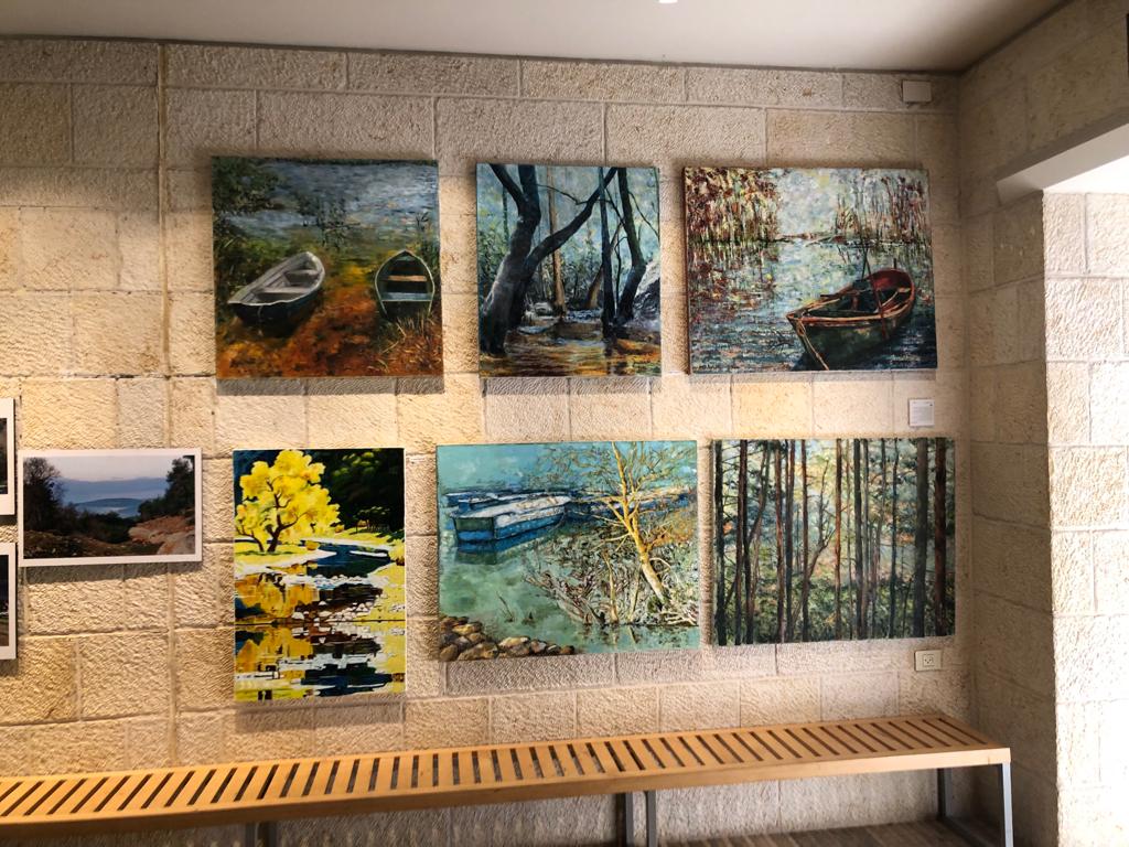 Landscape paintings hang in two rows on a pale stone wall above a long wooden bench.