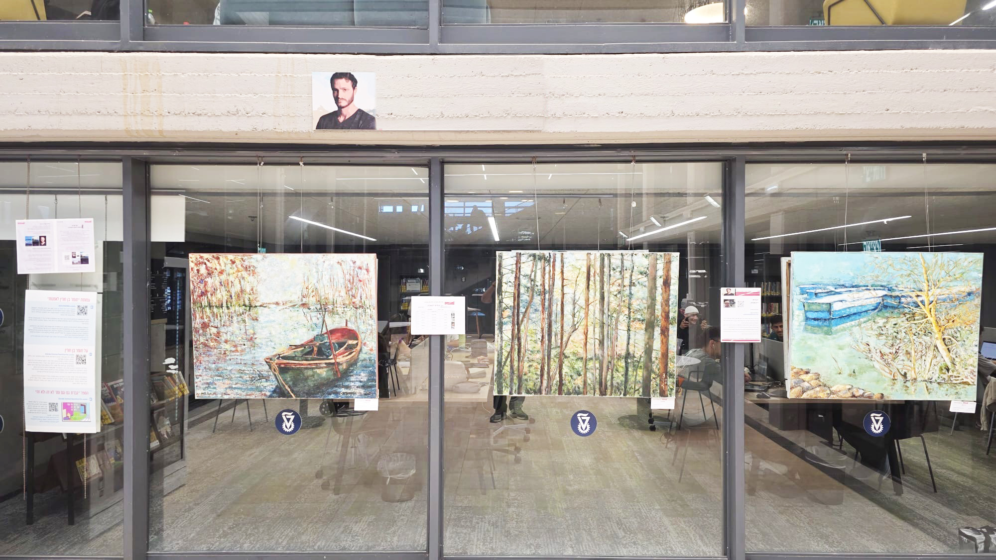 Several large paintings hang across a glass-fronted exhibition space, including a rowboat and tall woodland trees.