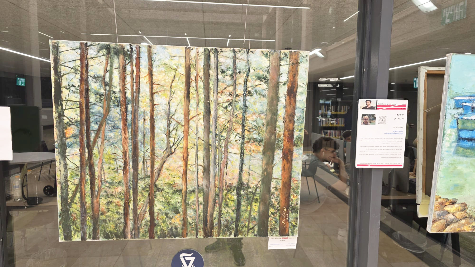 A woodland painting hangs against a glass panel, with tall slender trees, reflected corridor details and a label alongside.